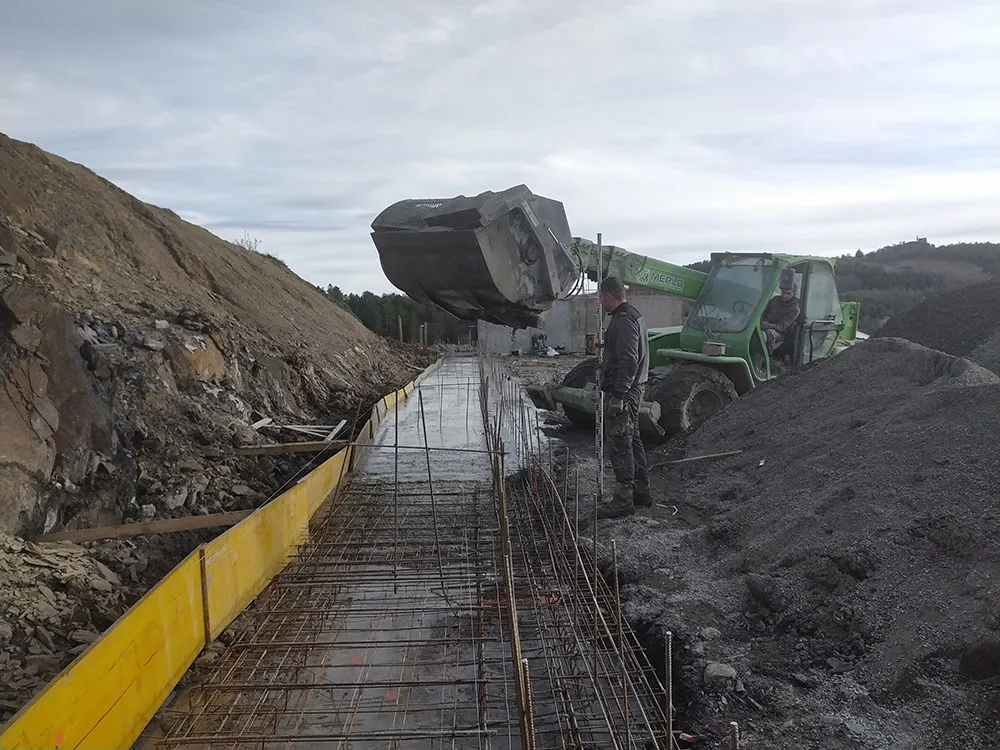 Coulage du béton au godet malaxeur dans une tranchée ferraillée à Upaix