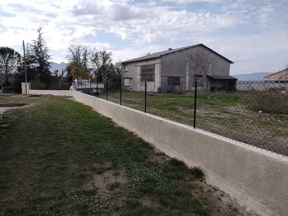 Grillage souple sur piquets posé au-dessus du muret de clôture enduit à Sisteron