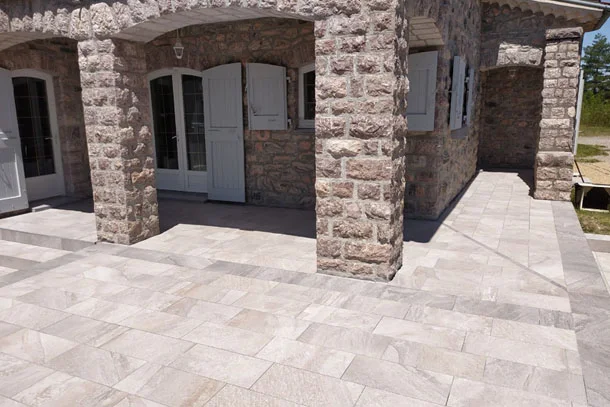 Terrasse dallée en pierre le long d'une façade en pierre à arcades avec volets